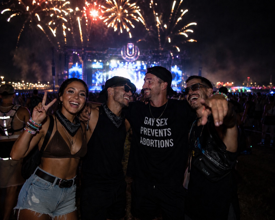 A group wearing the GAY SEX PREVENTS ABORTIONS t-shirt, laughing together under fireworks